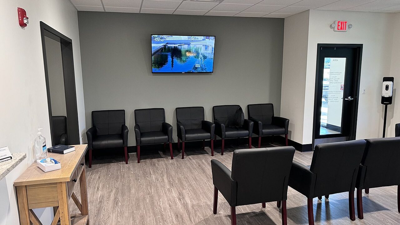 An empty, modern clinic waiting room with chairs arranged along the walls.