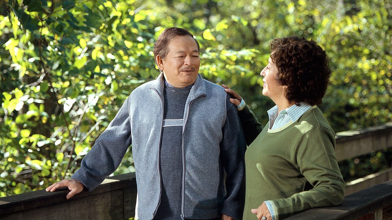 Two adults walking together outdoors beside green foliage.