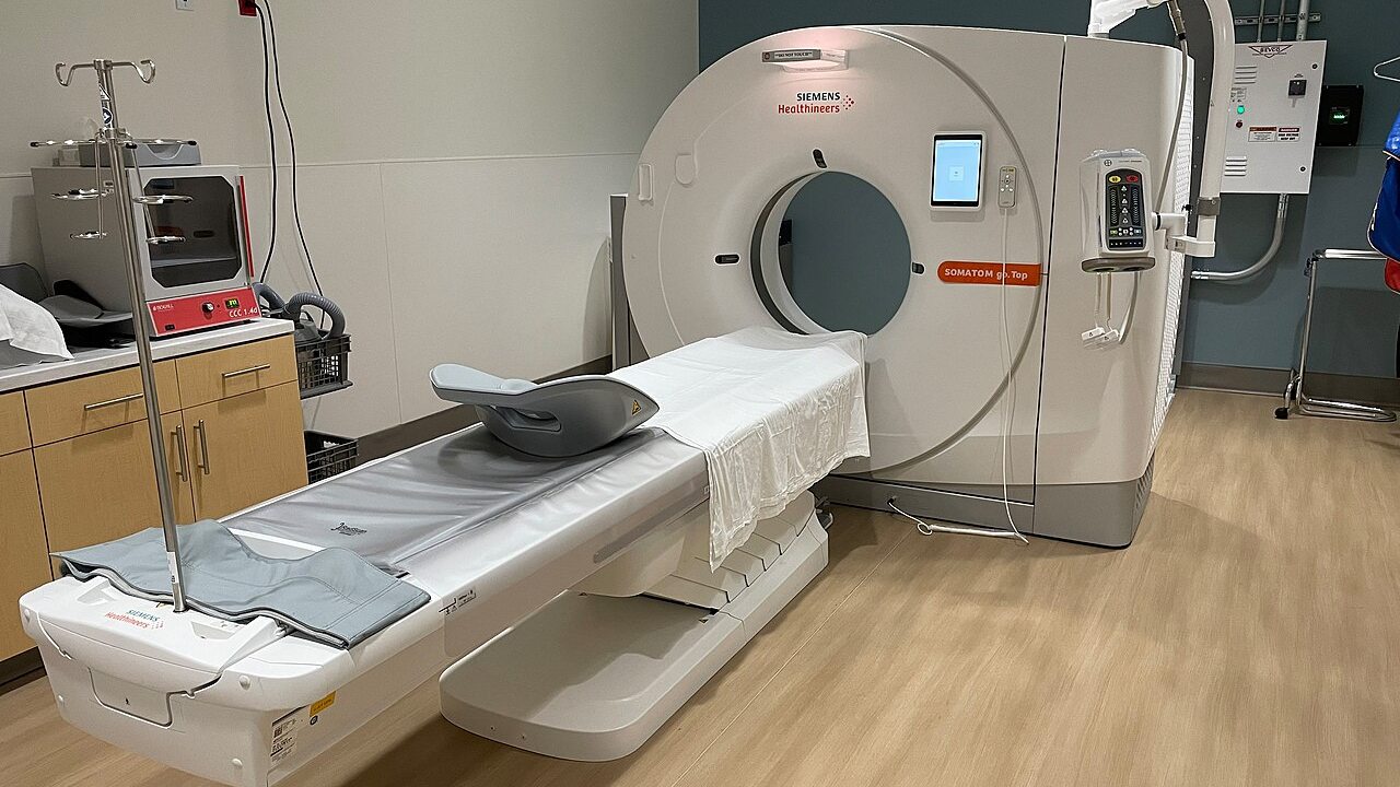 A modern CT scanner and patient table in an empty hospital imaging room.