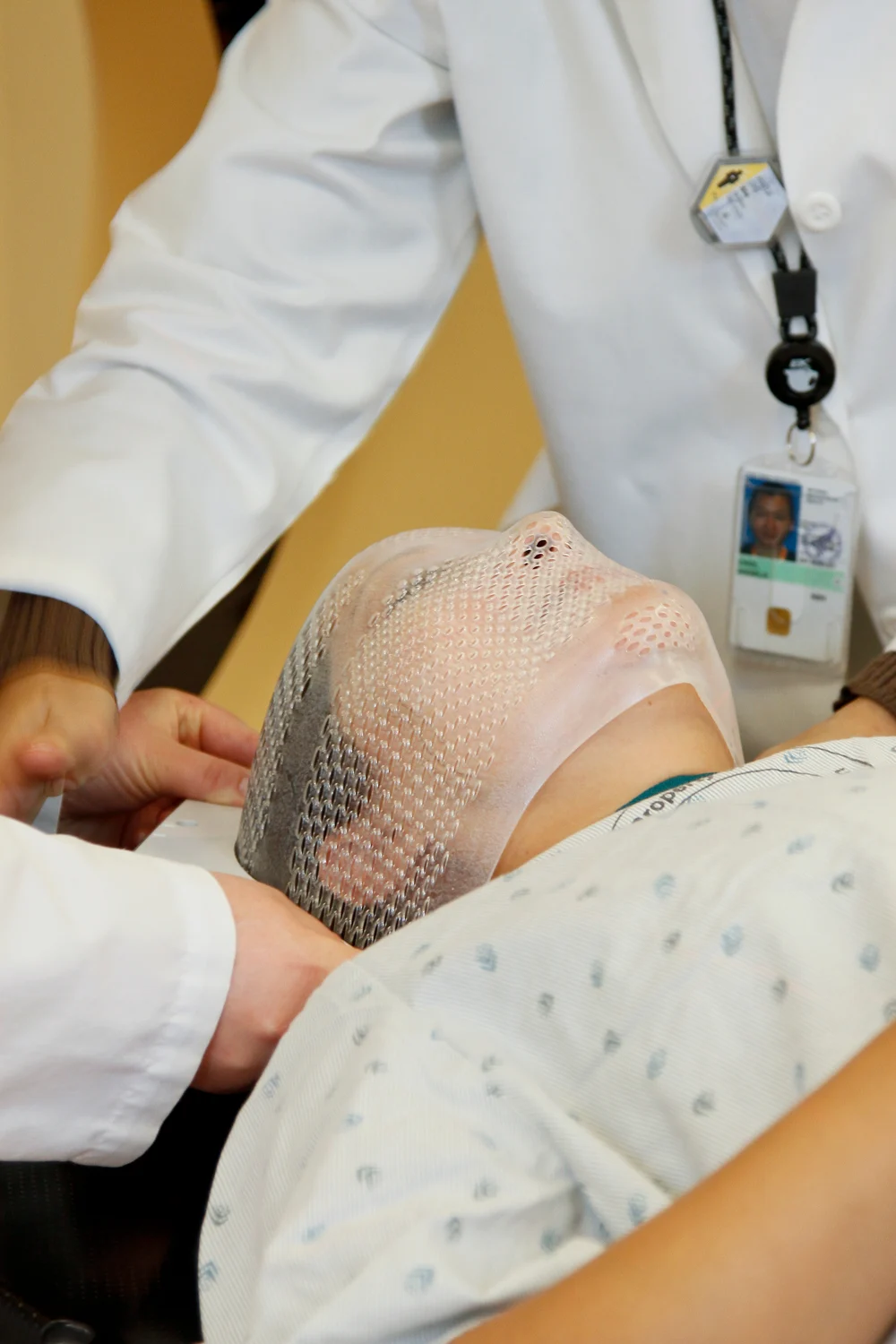 Radiation therapists fitting a mesh face mask to a patient model for radiotherapy positioning.