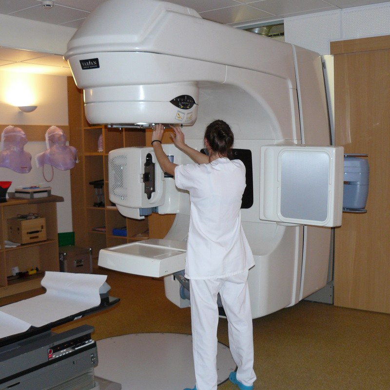 A radiotherapy professional preparing a medical linear accelerator in a treatment room.