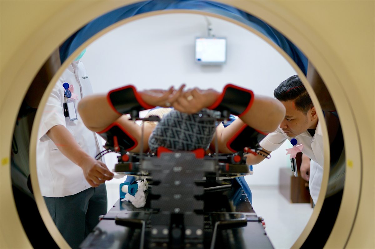Two radiotherapy professionals positioning a person on a support inside a CT scanner for breast radiotherapy simulation.
