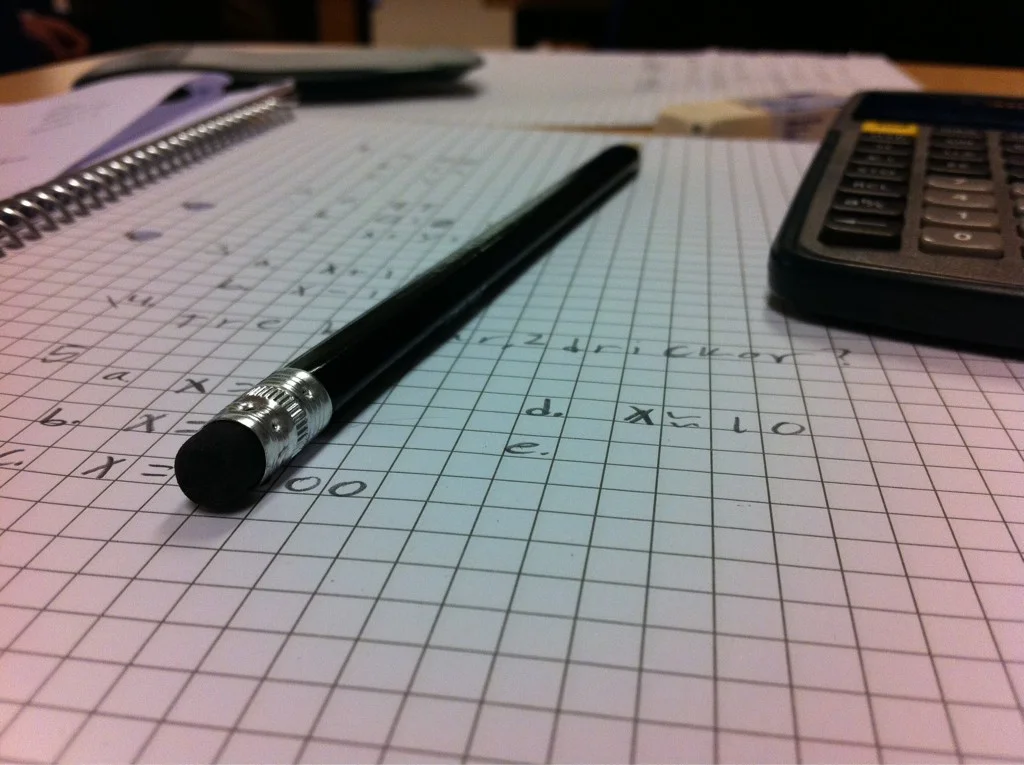 A pencil, calculator and handwritten arithmetic in a squared notebook.